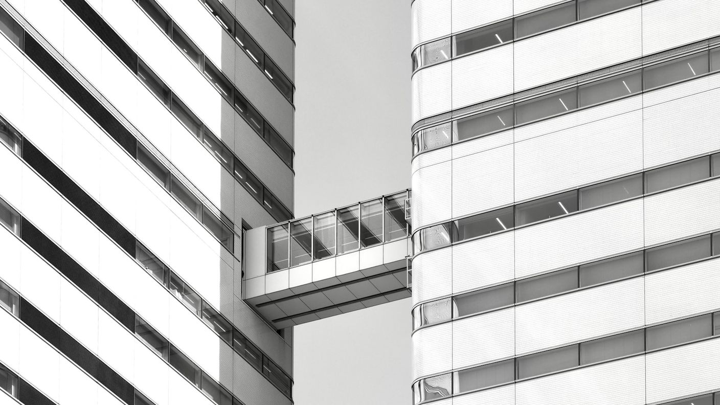 Glass sky bridge connecting two striped, layered building facades, echoing the application layer that connects company knowledge to AI engines